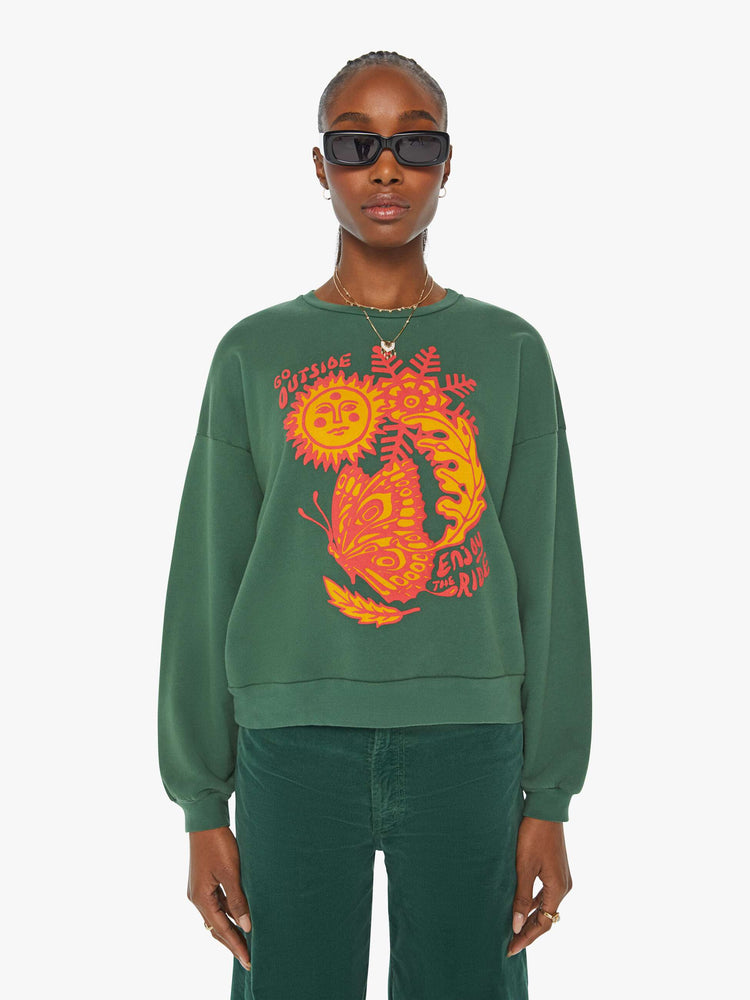 Front view of a woman in a green crewneck sweatshirt designed with a puff-paint graphic sun, butterfly and leaves on the front.