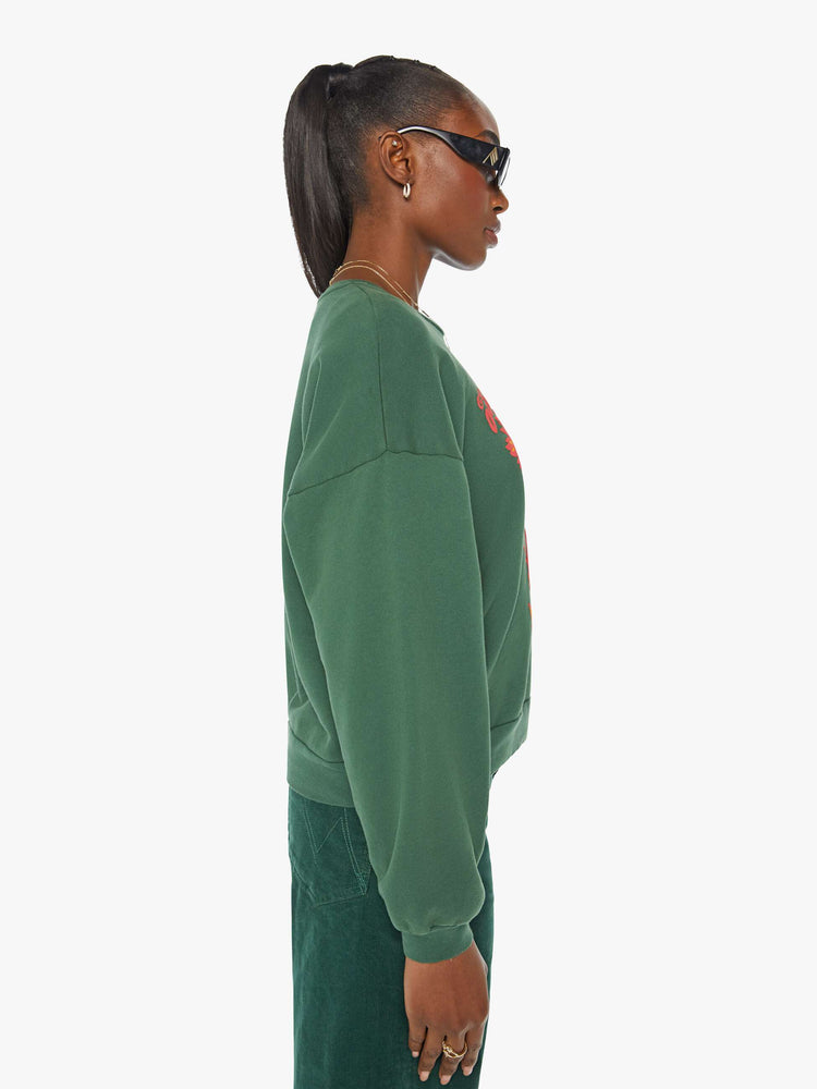 Side view of a woman in a green crewneck sweatshirt designed with a puff-paint graphic sun, butterfly and leaves on the front.