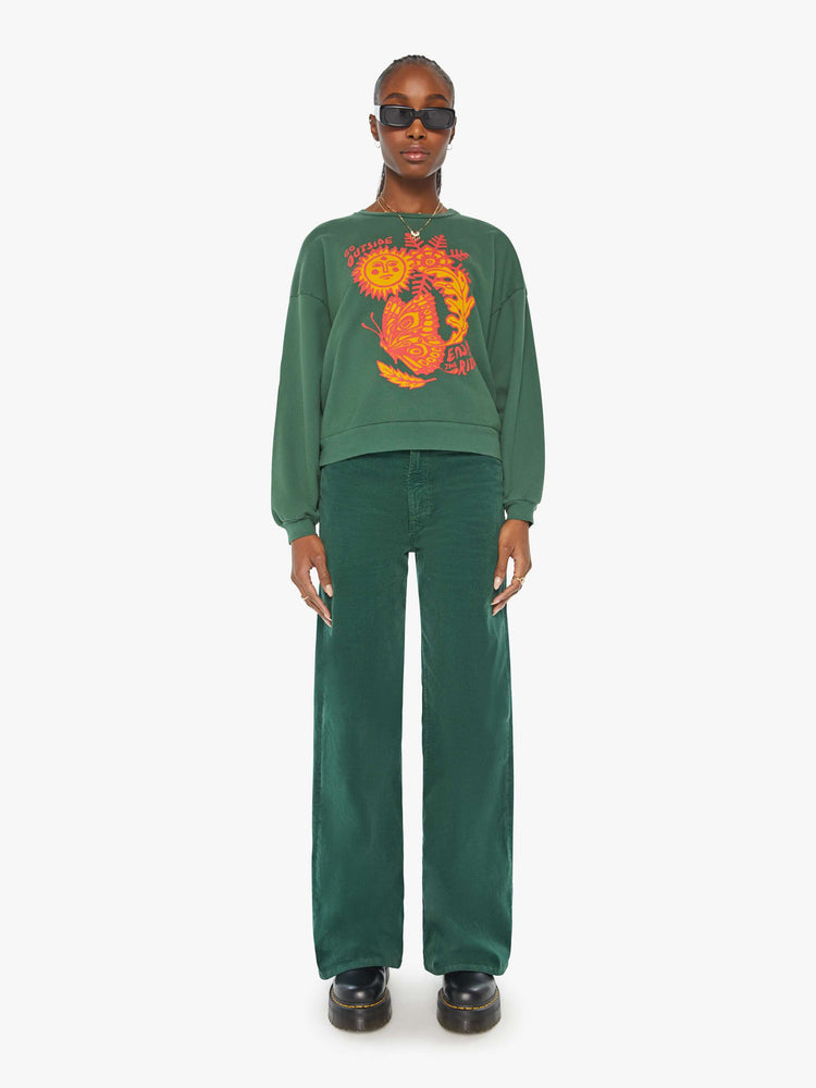 Full front view of a woman in a green crewneck sweatshirt designed with a puff-paint graphic sun, butterfly and leaves on the front.