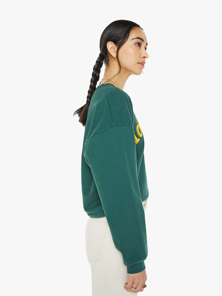 Side view of a woman in a green sweatshirt dropped sleeves and a relaxed fit.