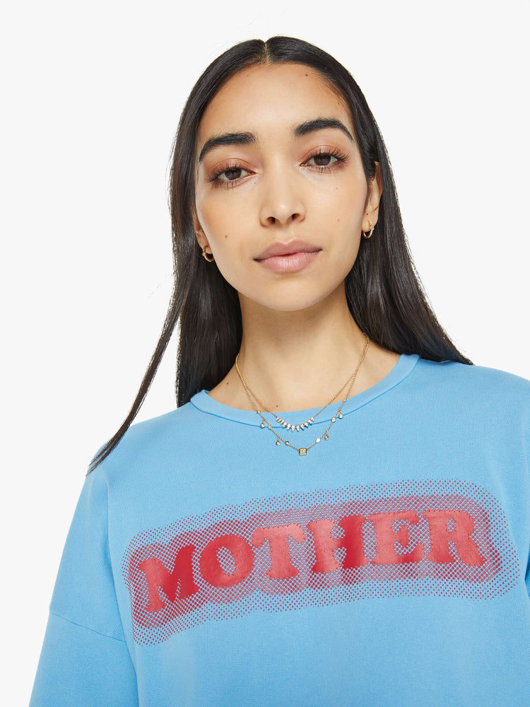 Close up view of a woman in crewneck sweatshirt with dropped sleeves in light blue with MOTHER's name in red.