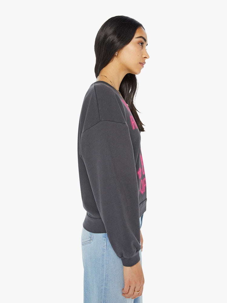 Side view of a woman in a faded black sweatshirt with a text graphic in hot pink on the front inspired by a psychic shop's neon sign.