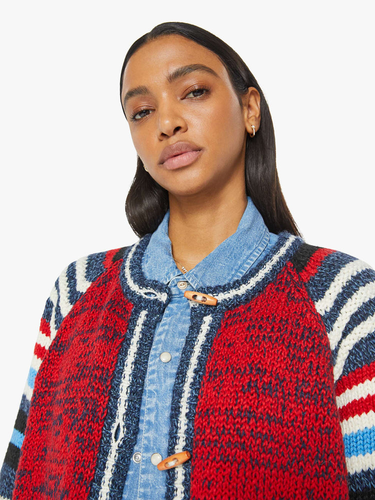 Close up view of a woman in an  oversized raglan cardigan with patch pockets, long balloon sleeves and ribbed hems in a marled red and navy knit with striped details and vintage-inspired wooden buttons. 