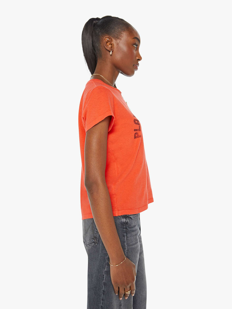 Side view of a woman in an orange crewneck with a slim designed with a faded graphic on the front.