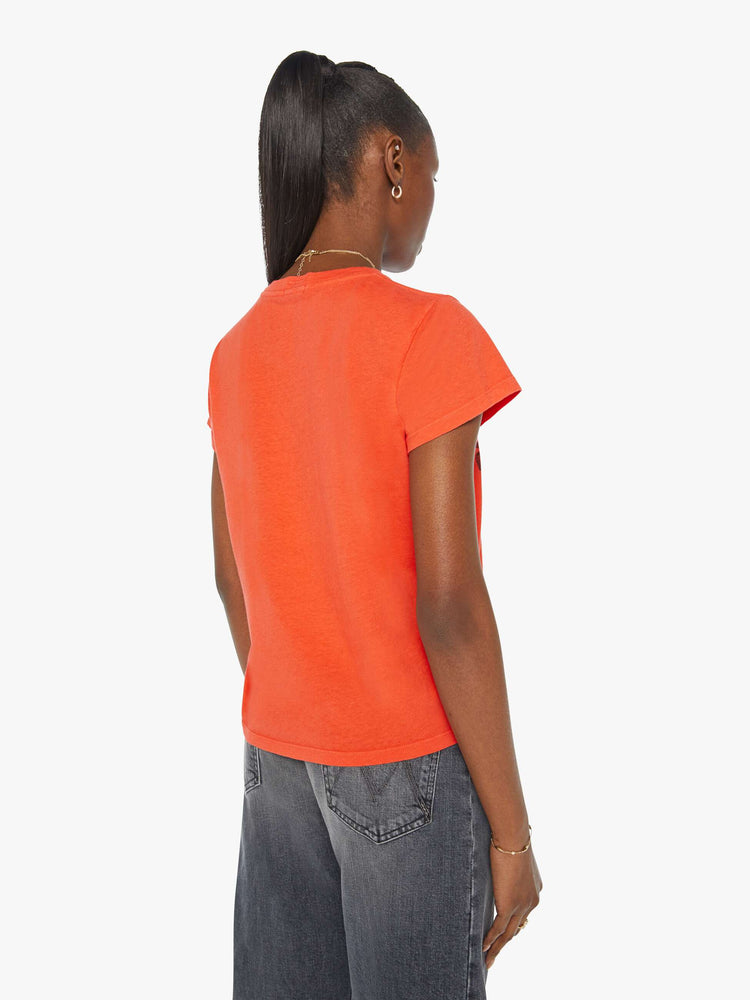 Back view of a woman in an orange crewneck with a slim designed with a faded graphic on the front.