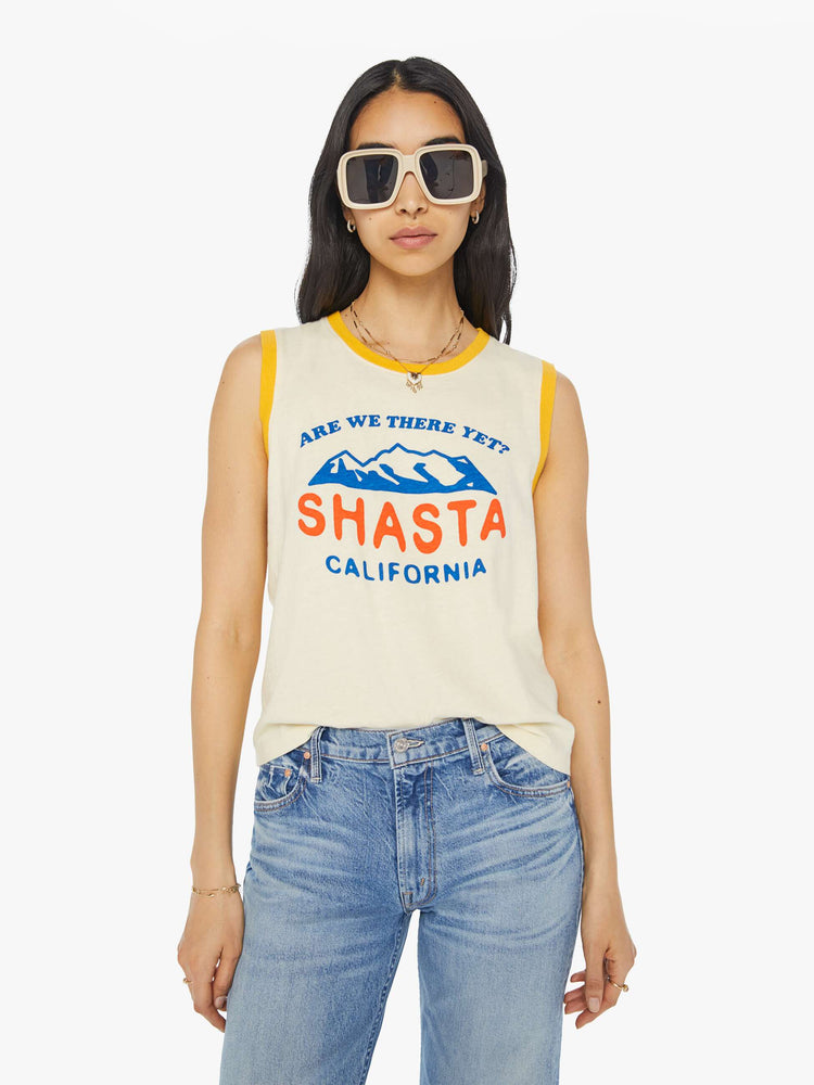 Front view of a woman in a cropped muscle tee with a crewneck and boxy fit in a cream tank with vintage inspired graphic with yellow trim.