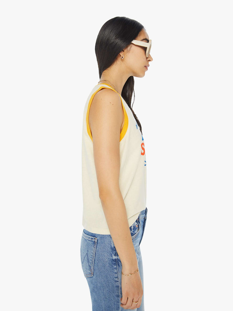 Side view of a woman in a cropped muscle tee with a crewneck and boxy fit in a cream tank with vintage inspired graphic with yellow trim.