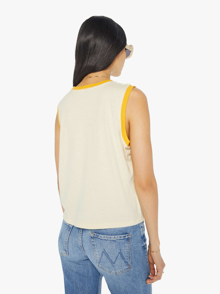 Back view of a woman in a cropped muscle tee with a crewneck and boxy fit in a cream tank with vintage inspired graphic with yellow trim.