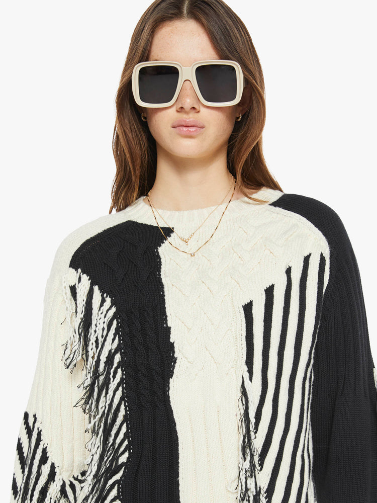 Close up view of a woman crewneck sweater with drop shoulders, ribbed hems and a cropped, boxy fit in a cream and black geometric panels and fringe details.