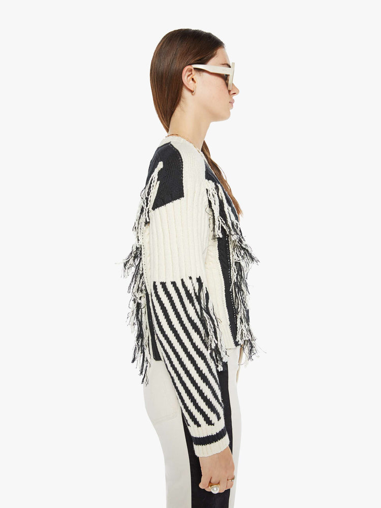 Side view of a woman crewneck sweater with drop shoulders, ribbed hems and a cropped, boxy fit in a cream and black geometric panels and fringe details.