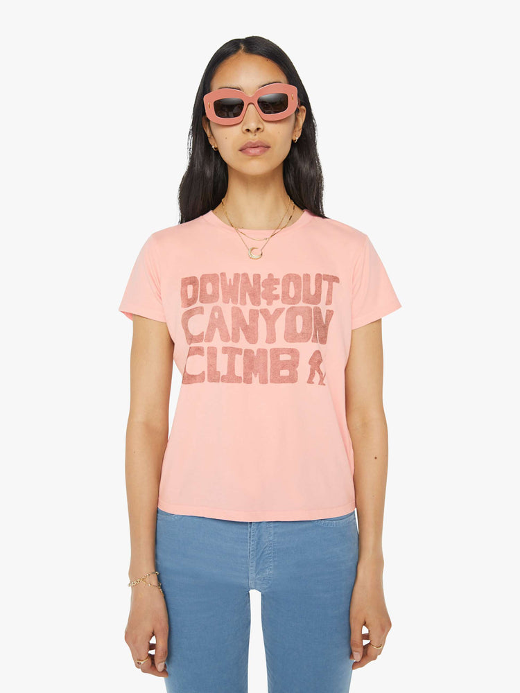 Front view of a woman in a sheer baby pink crewneck tee with a slim featuring a faded text graphic on the front.