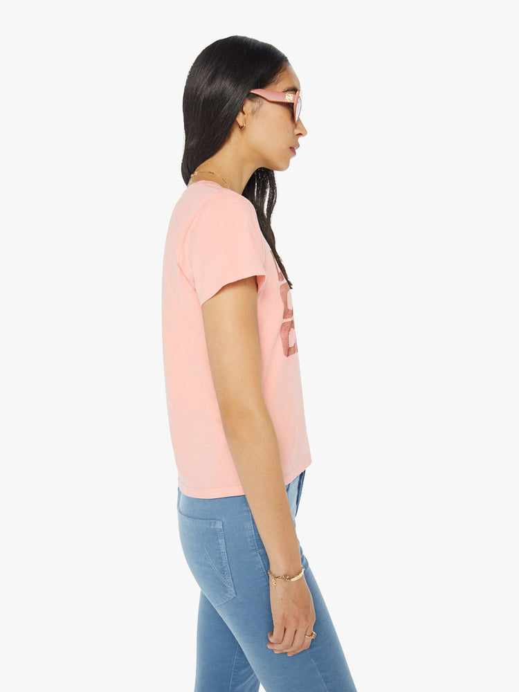 Side view of a woman in a sheer baby pink crewneck tee with a slim fit featuring a faded text graphic on the front.