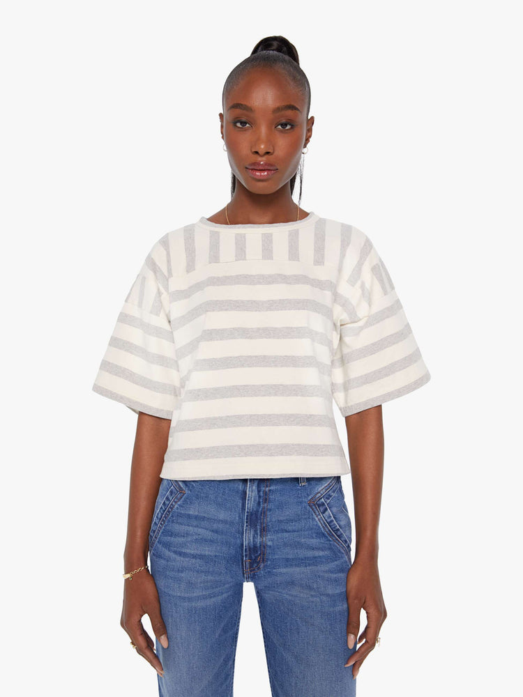 Front view of a woman in a box top with dramatic drop shoulders, short sleeves and a slightly cropped hem in off-white and grey horizontal stripes.