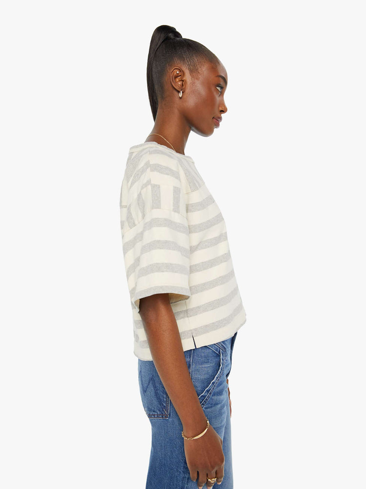 Side view of a woman in a box top with dramatic drop shoulders, short sleeves and a slightly cropped hem in off-white and grey horizontal stripes.