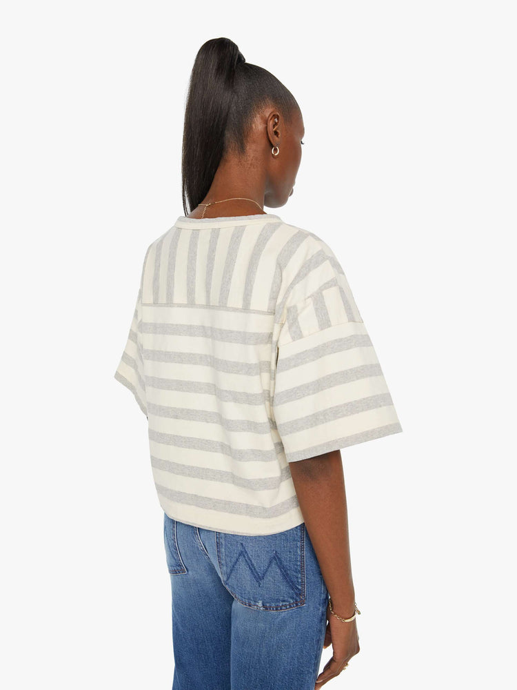 Back view of a woman in a box top with dramatic drop shoulders, short sleeves and a slightly cropped hem in off-white and grey horizontal stripes.