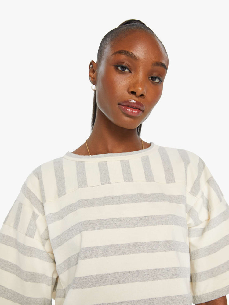 Close up view of a woman in a box top with dramatic drop shoulders, short sleeves and a slightly cropped hem in off-white and grey horizontal stripes.