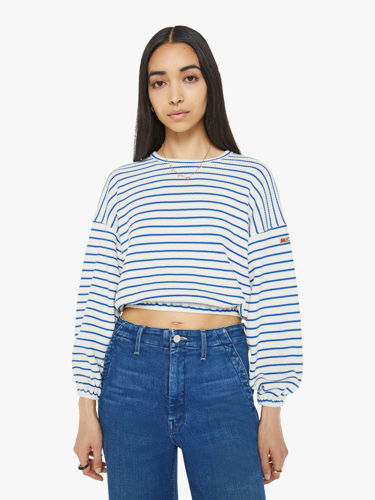 Front view of woman in a cream with blue stripes cropped long sleeve top with a crew neck, drop shoulders and elastic hems.