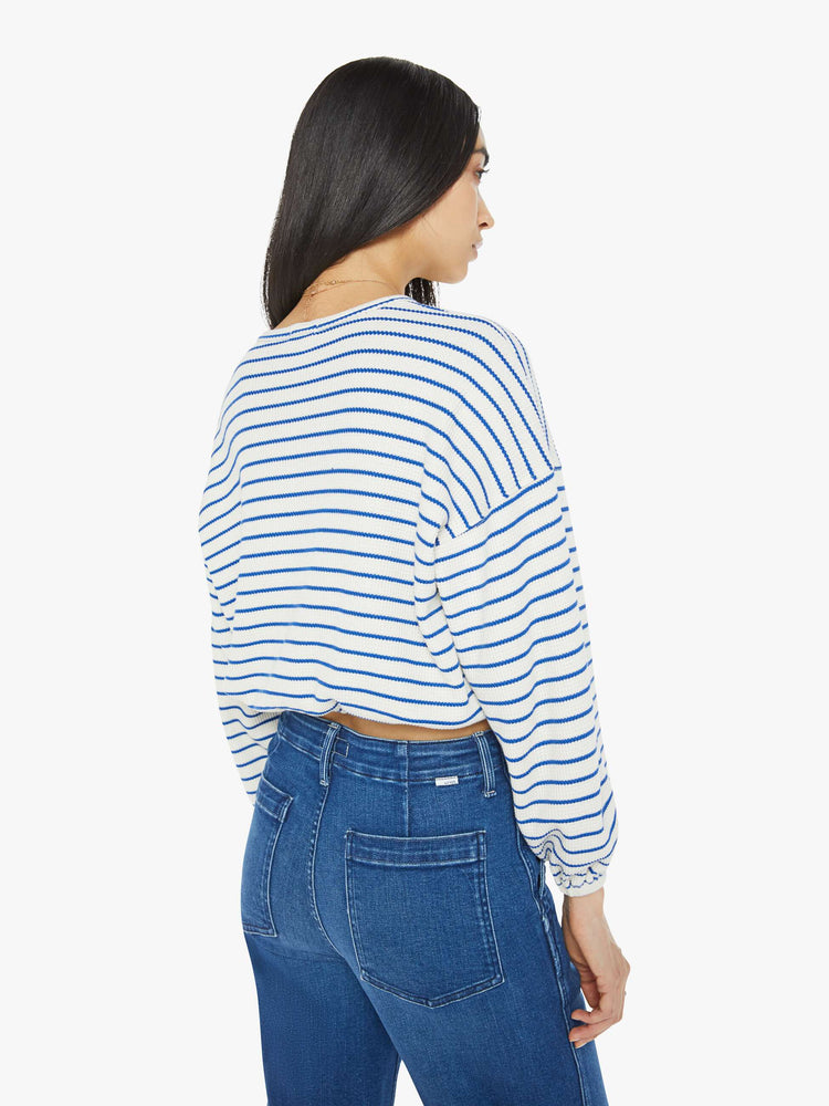 Back view of woman in a cream with blue stripes cropped long sleeve top with a crew neck, drop shoulders and elastic hems.