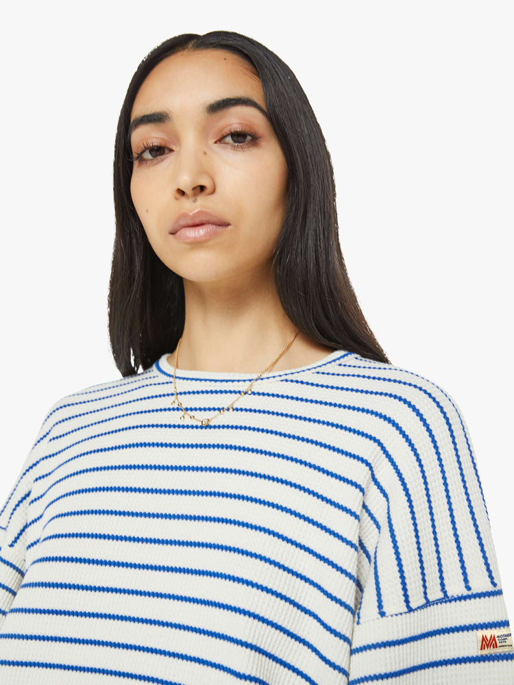 Close up view of woman in a cream with blue stripes cropped long sleeve top with a crew neck, drop shoulders and elastic hems.