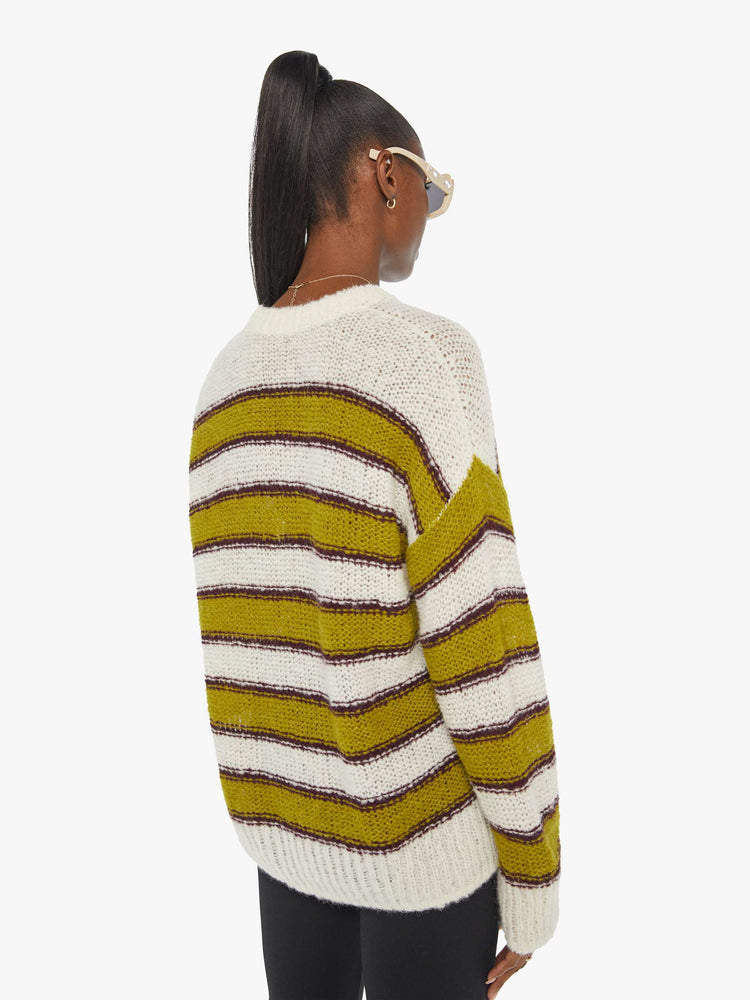 Back view of woman in an oversized crewneck sweater with dramatic drop shoulders, extra long sleeves and thick ribbed hems in a green, maroon and cream horizontal stripe pattern.