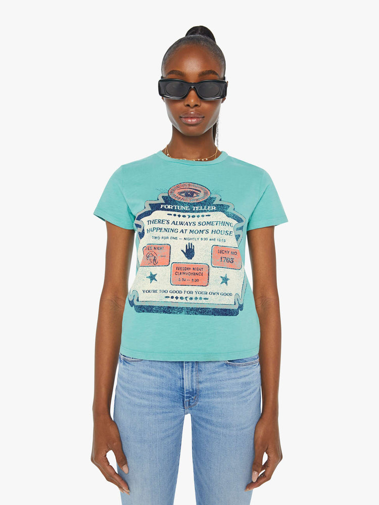 Front view of a woman in a teal tee that features a faded graphic inspired by a fortune teller advertisement on the front and text on the back.