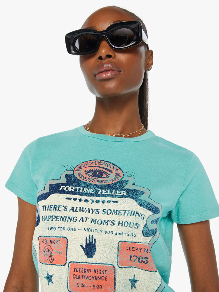 Close view of a woman in a teal tee that features a faded graphic inspired by a fortune teller advertisement on the front and text on the back.