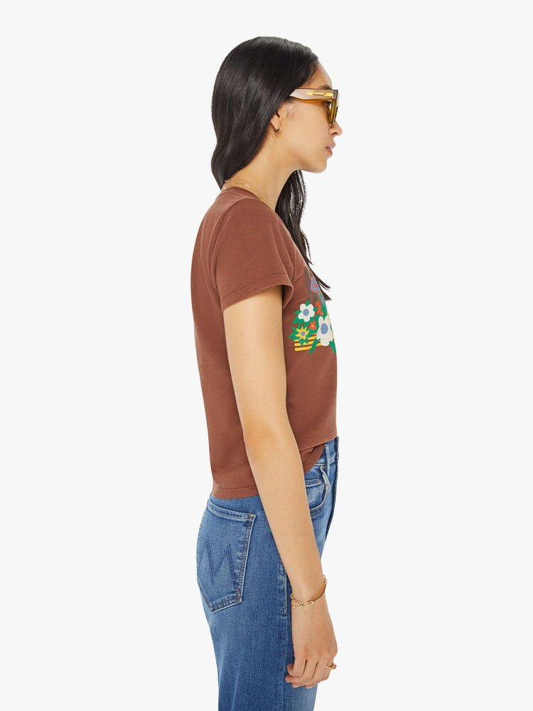 Side view of a woman in a brown crewneck tee with a slim fit featuring a colorful garden bed graphic on the front.