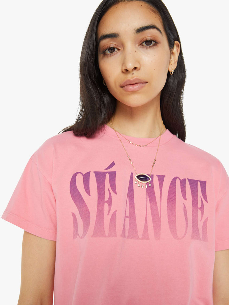 Close up view of a pink oversized crewneck tee with drop shoulders, a cropped hem and a boxy fit and purple print.