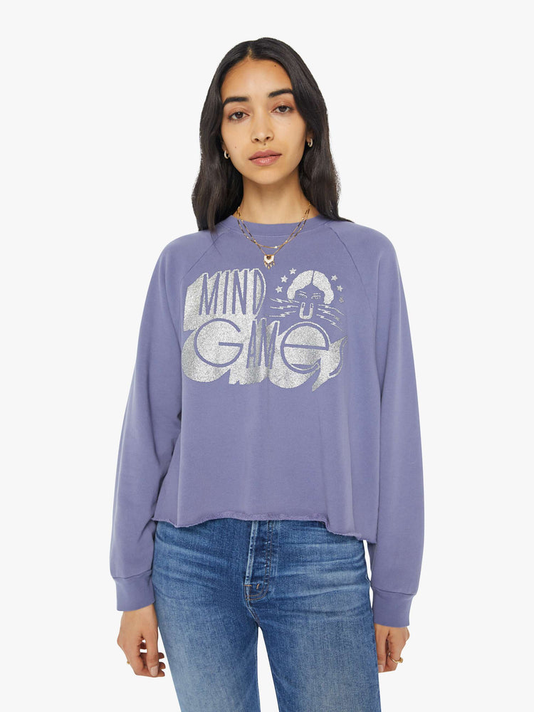 Front view of a woman in a cropped sweatshirt with a crew neck, drop shoulders and a raw hem in a lavender color with a silver graphic.