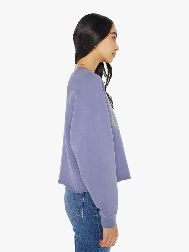 Side view of a woman in a cropped sweatshirt with a crew neck, drop shoulders and a raw hem in a lavender color with a silver graphic.