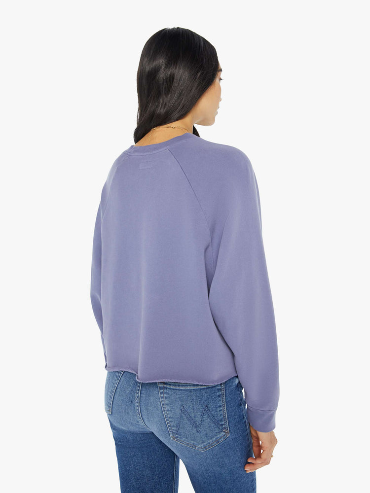 Back view of a woman in a cropped sweatshirt with a crew neck, drop shoulders and a raw hem in a lavender color with a silver graphic.