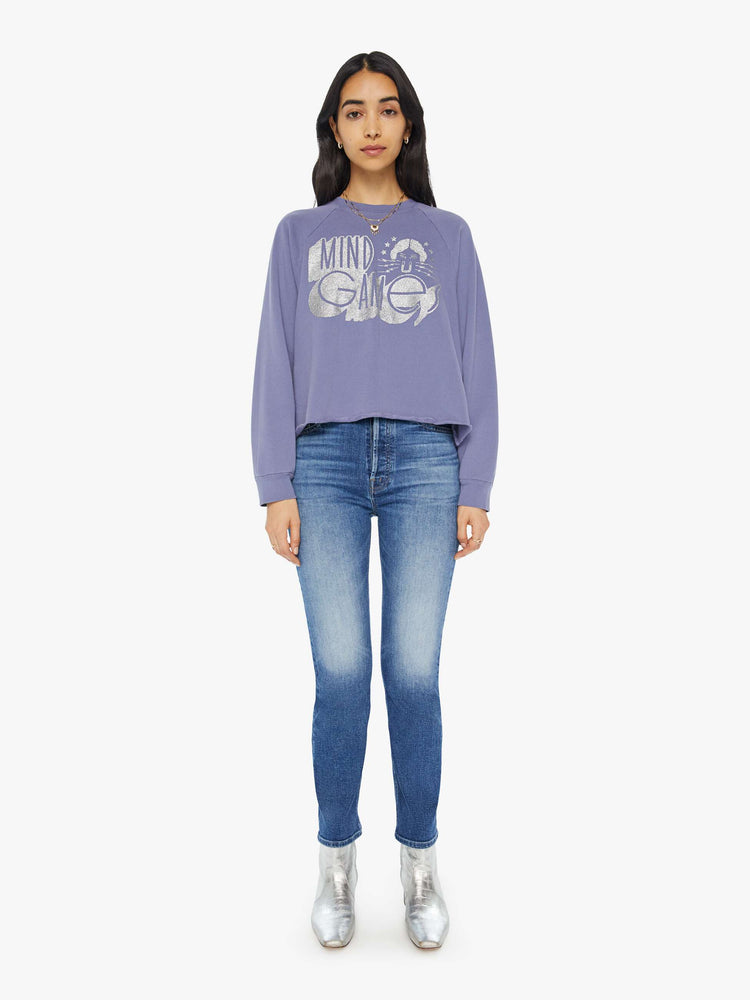 Full body view of a woman in a cropped sweatshirt with a crew neck, drop shoulders and a raw hem in a lavender color with a silver graphic.