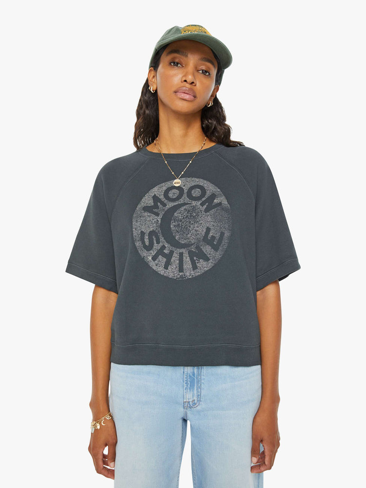 Front view of a woman dark grey  short sleeve raglan sweatshirt with ribbed hems and a loose, boxy fit with a faded moon graphic with text in white on the front.