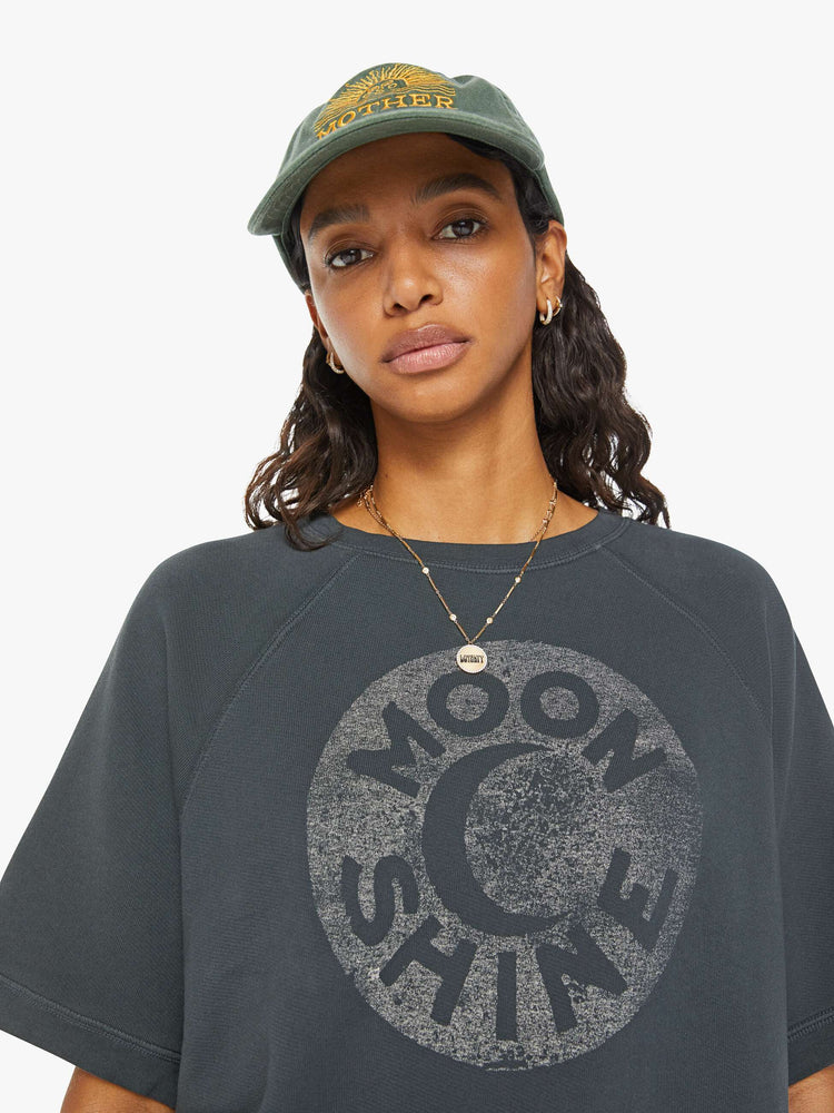 Close up view of a woman dark grey short sleeve raglan sweatshirt with ribbed hems and a loose, boxy fit with a faded moon graphic with text in white on the front.