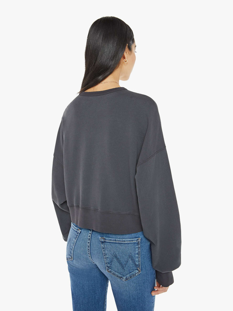 Back view of a woman in a faded black  sweatshirt with drop shoulders, super long sleeves, ribbed hems and a wide, cropped fit with pink text on front.