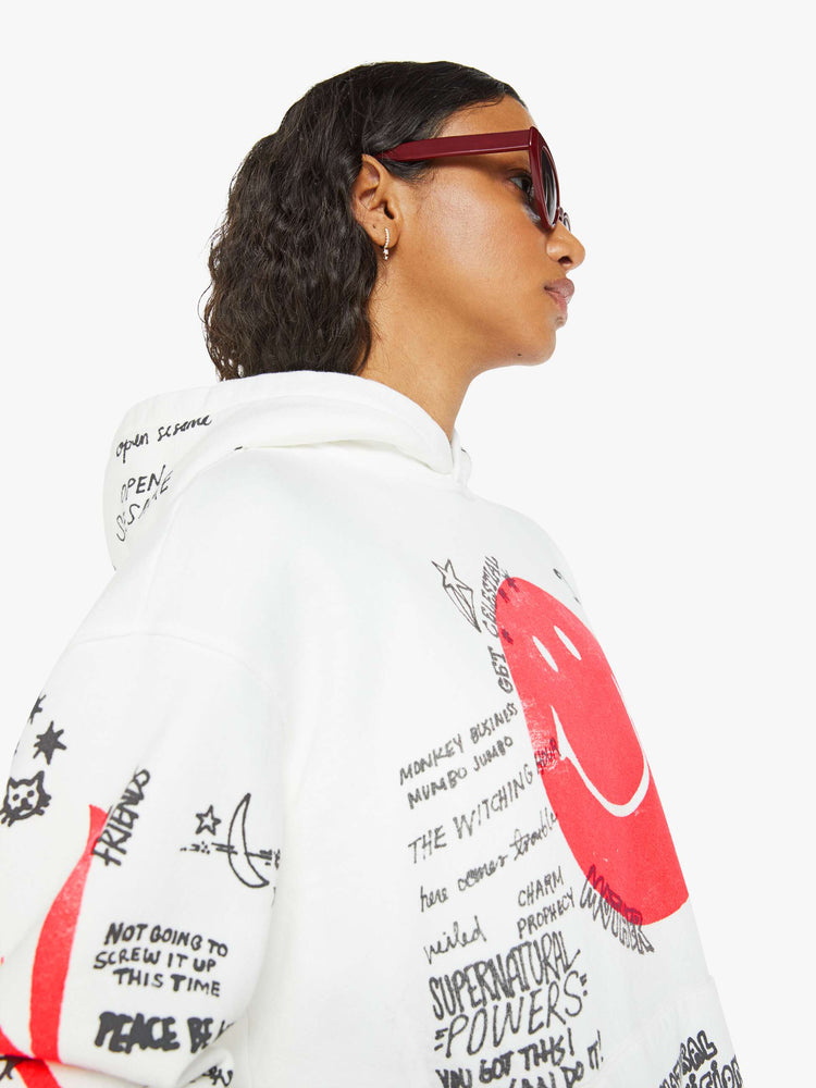 Close up view of a woman in a classic hoodie with drop shoulders, a front patch pocket and ribbed hems in white  and red smiley face with drawn scribbles.