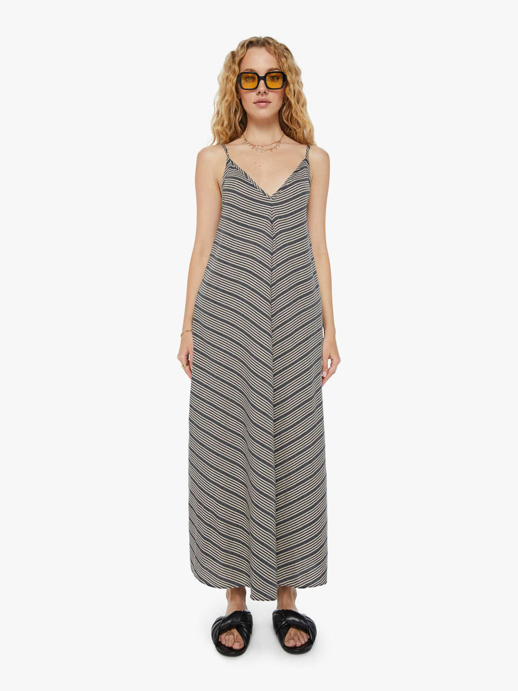 Front view of a woman in a grey and white striped  maxi dress with a V-neck, thin spaghetti straps that tie in the back, an ankle-length hem and a flowy fit. 