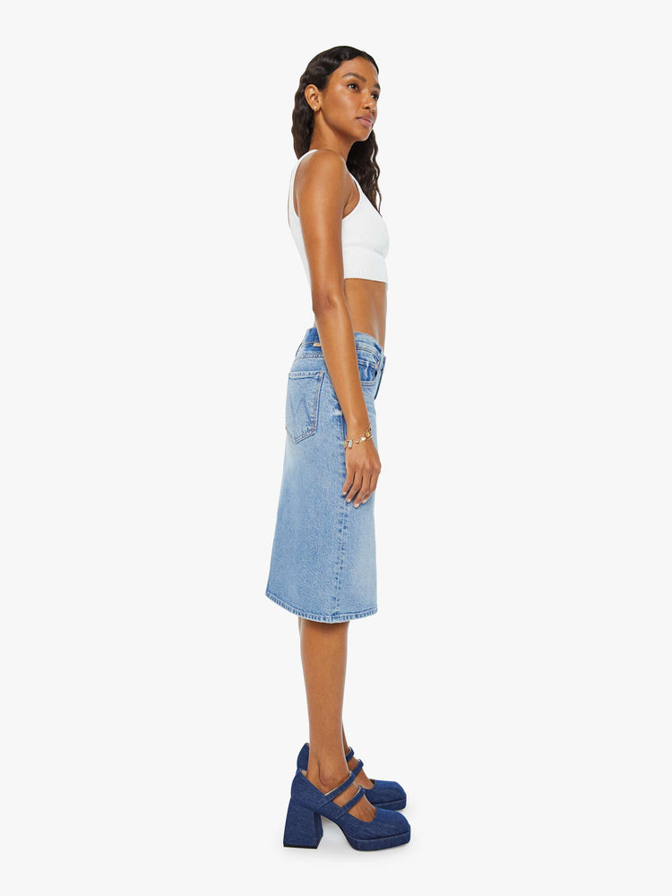 Side view of a woman in light blue denim midi skirt with a button fly and relaxed fit that's designed to sit on the hips. 