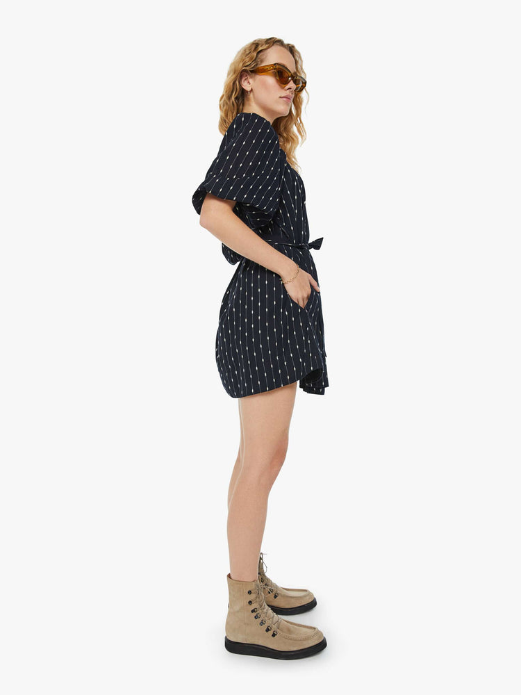 Side view of a woman square neck mini dress with elbow-length balloon sleeves, buttons down the chest, an elastic waistband and a thigh-grazing hem in black with white stripes and polda dots.