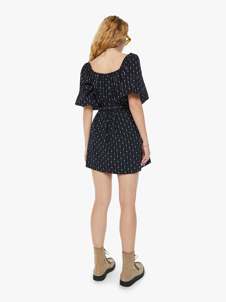 Back view of a woman square neck mini dress with elbow-length balloon sleeves, buttons down the chest, an elastic waistband and a thigh-grazing hem in black with white stripes and polda dots.