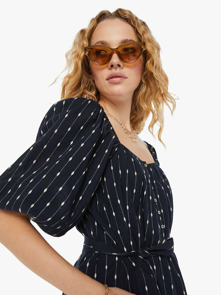 Close up view of a woman square neck mini dress with elbow-length balloon sleeves, buttons down the chest, an elastic waistband and a thigh-grazing hem in black with white stripes and polda dots.