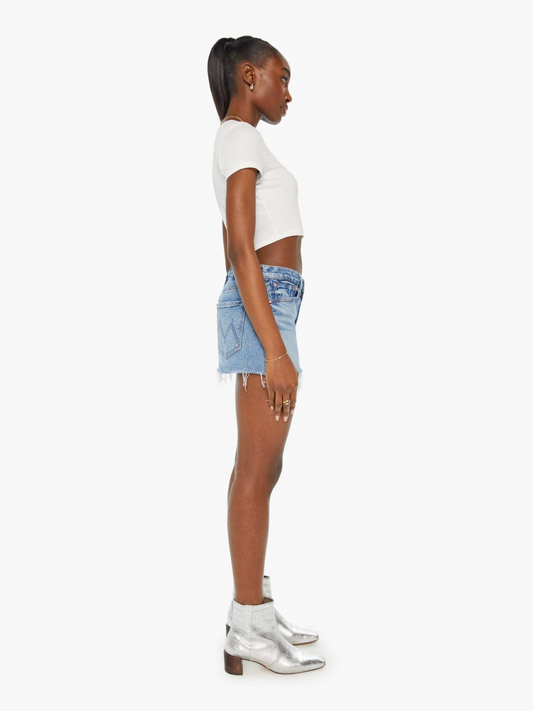 Side view of a woman super-short denim mini skirt with exposed pocket liners and a frayed hem in a light blue wash.