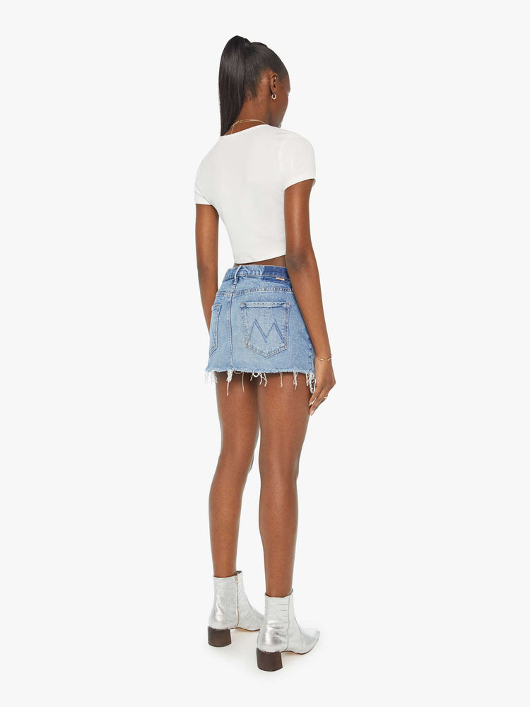 Back view of a woman super-short denim mini skirt with exposed pocket liners and a frayed hem in a light blue wash.