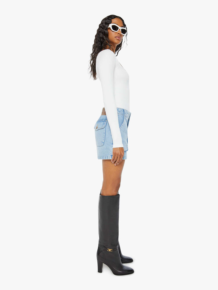 Side view of a woman in a light blue denim mini skirt with a zip fly, raised pockets and a clean hem. 