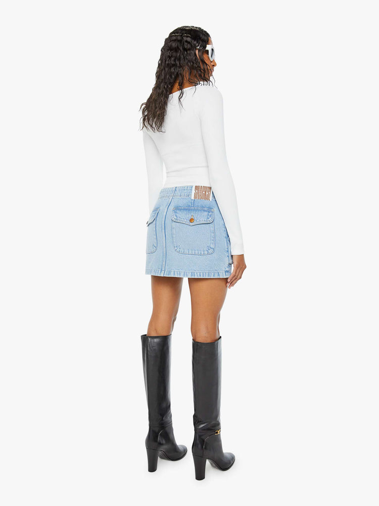 Back view of a woman in a light blue denim mini skirt with a zip fly, raised pockets and a clean hem. 