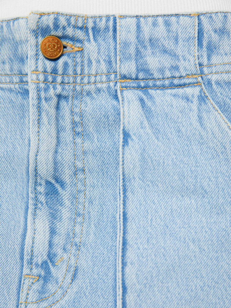 Detailed view of a woman in a light blue denim mini skirt with a zip fly, raised pockets and a clean hem. 