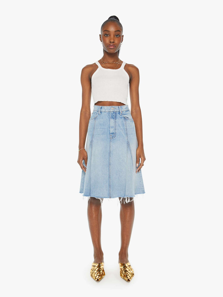 Front view of a woman in a high waisted denim midi skirt with slit pockets, seamed details down the front and raw hem in light blue denim.