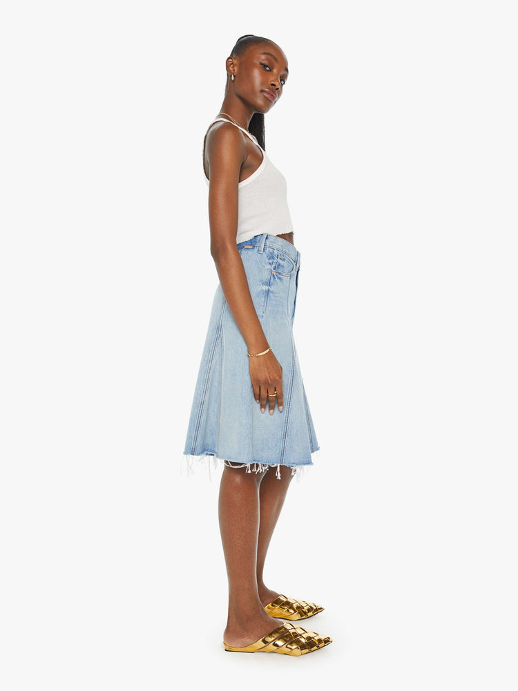 Side view of a woman in a high waisted denim midi skirt with slit pockets, seamed details down the front and raw hem in light blue denim.