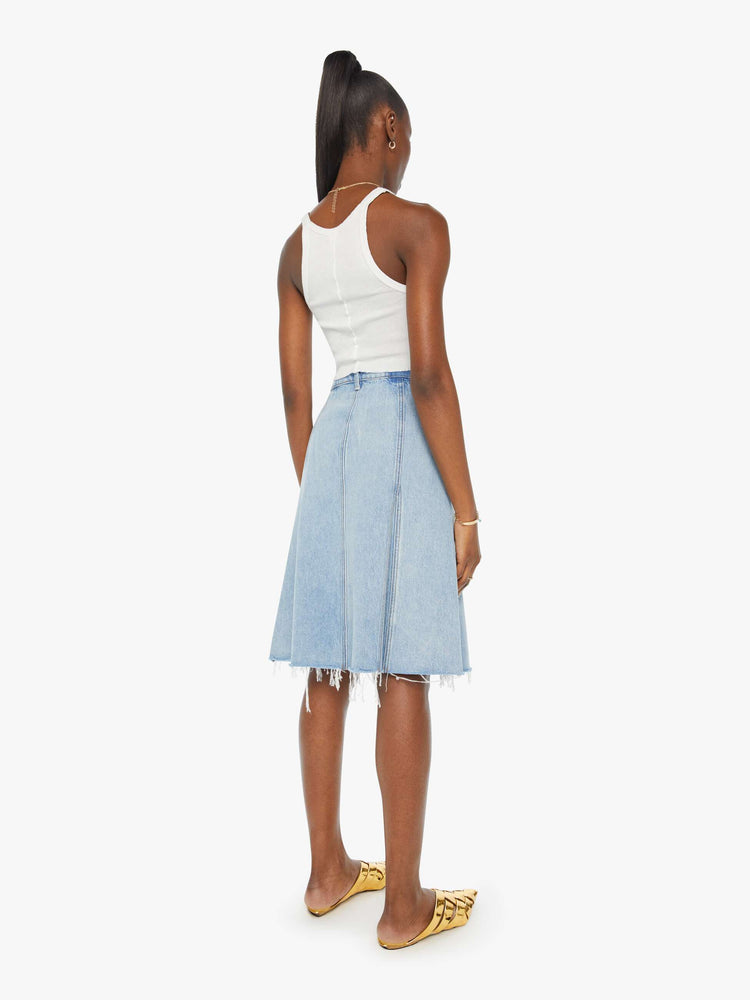 Back view of a woman in a high waisted denim midi skirt with slit pockets, seamed details down the front and raw hem in light blue denim.