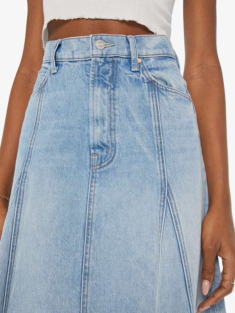 Close up view of a woman in a high waisted denim midi skirt with slit pockets, seamed details down the front and raw hem in light blue denim.